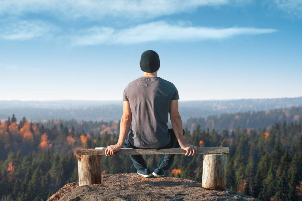 a person sits on a bench overlooking a mountain and forest during life after rehab