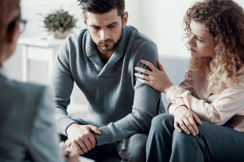 a couple comforts each other as they talk to a therapist about signs of heroin addiction