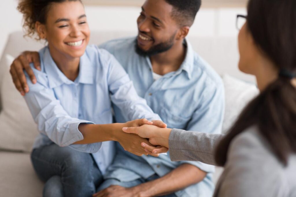 two people sit on a couch while one of them shakes hands with a counselor in a residential treatment program