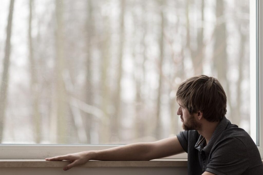 a person looks sadly out of a window possibly struggling with alcohol addiction vs dependence