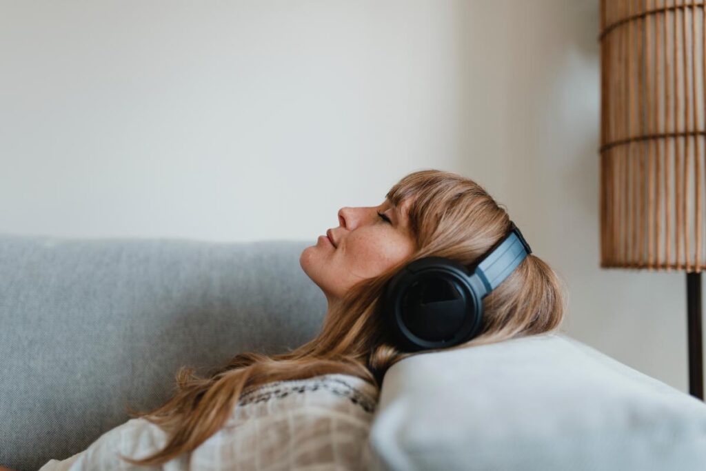 woman laying on bed with headphones listening to 5 songs about overcoming addiction
