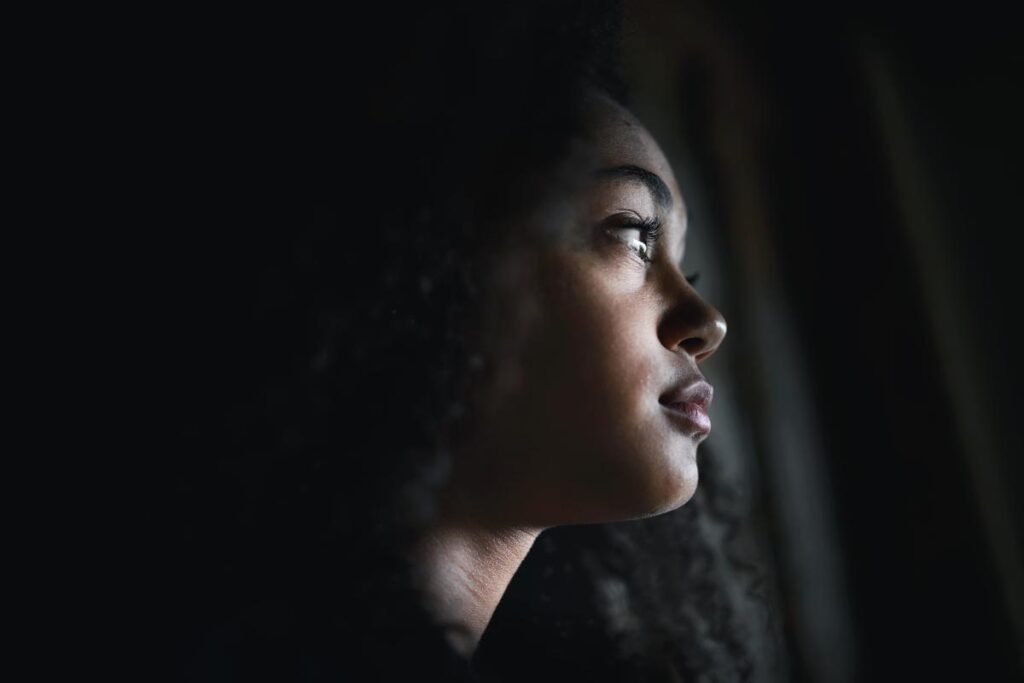 young woman in dimly lit room staring off into space recalling the 3 vivitrol side effects you should know about