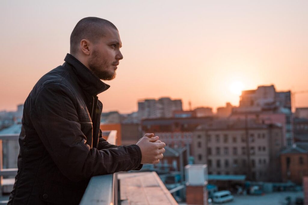 young man standing on rooftop overlooking city at sunset practicing lessons for a post anxiety attack and how to recover