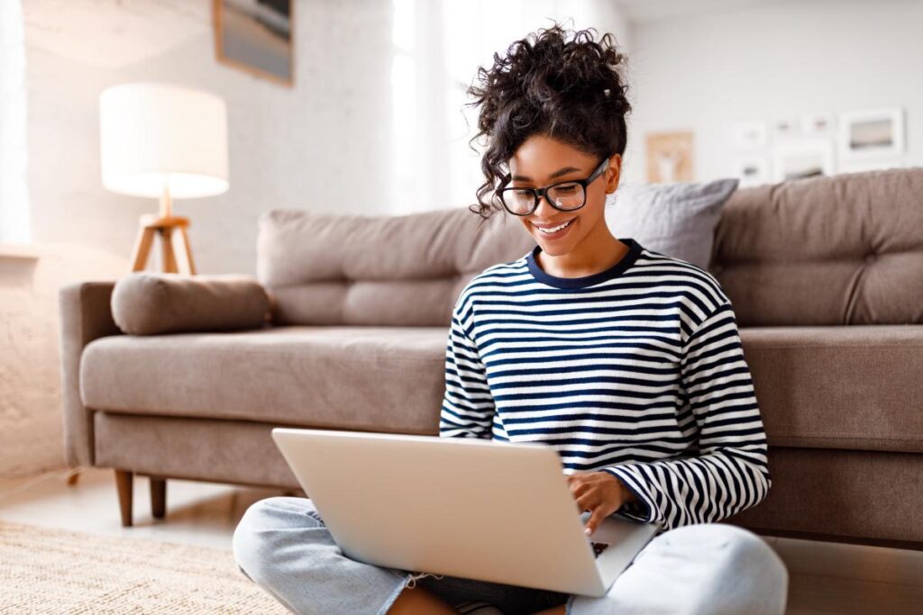 young, happy woman sitting on floor with laptop searching for the best online ptsd support groups