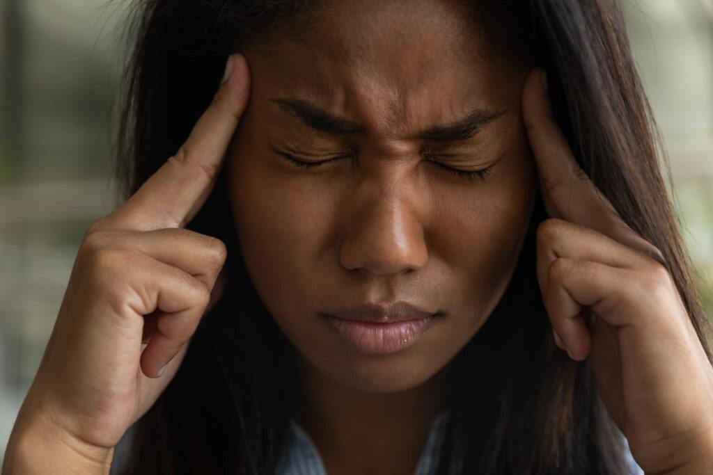 young woman grimacing in pain while holding her head asking what are the physical effects of heroin