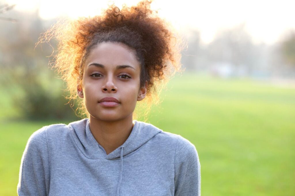 young woman looking seriously into the camera while standing outside in a field and asking what is vivitrol
