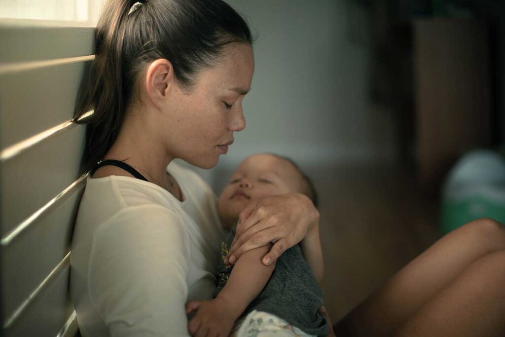 a person looks sad while holding a baby and wondering how long does postpartum depression last