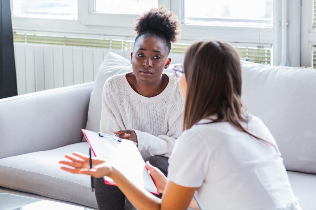 Patient on couch at detox program, talking to health professional holding clipboard