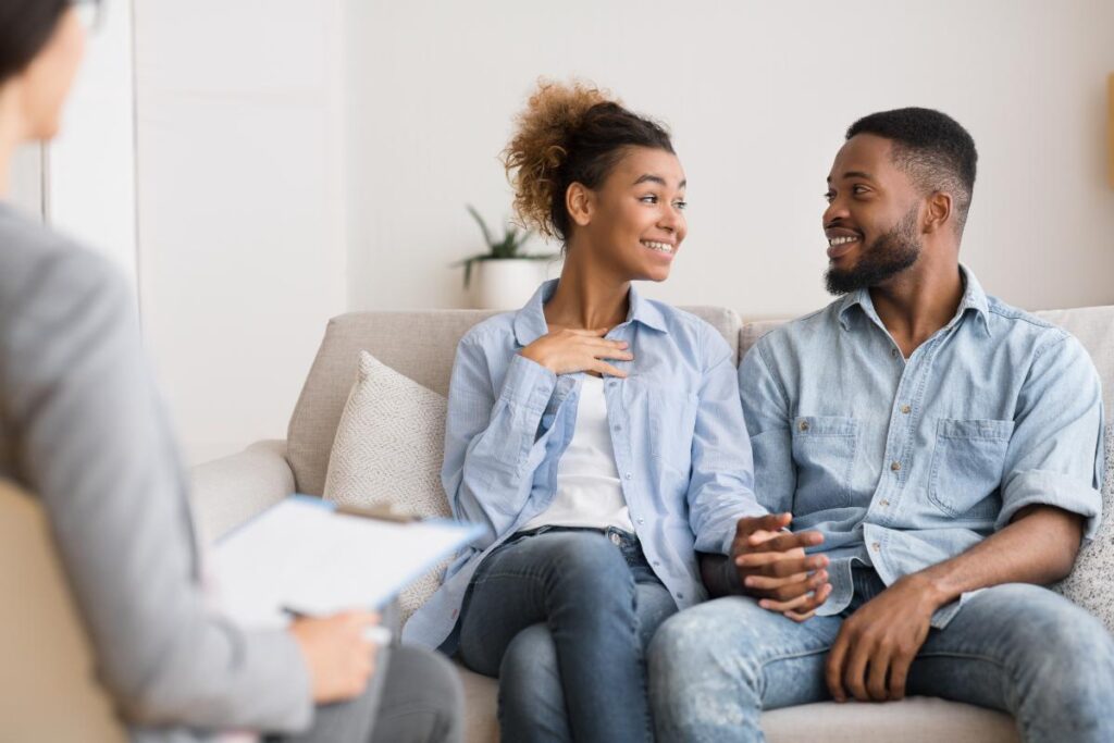 a couple sits with a therapists and holding hands as they are restoring relationships