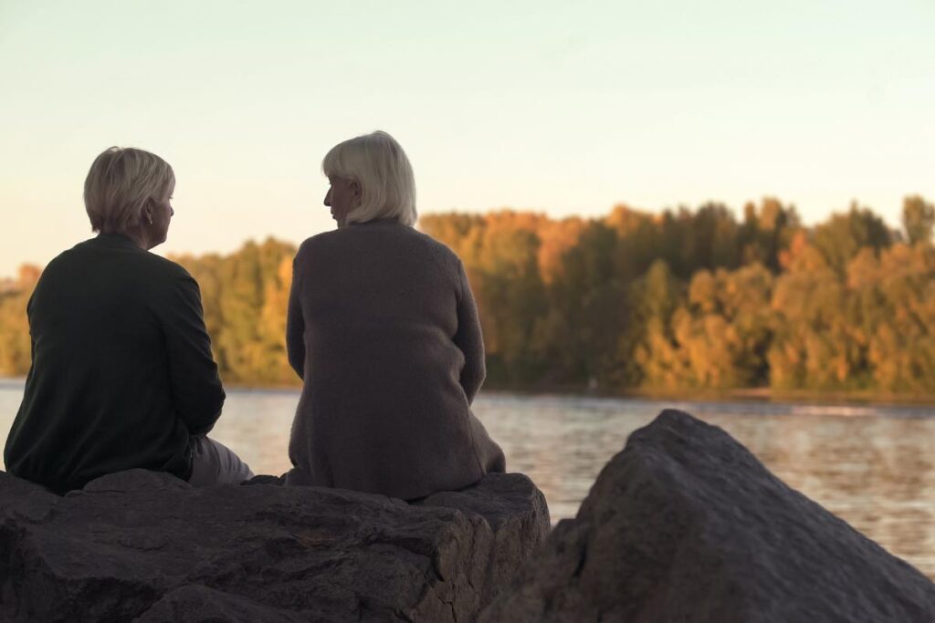 two elderly folks sit on a rock in front of a lake and talk about anxiety activities for adults