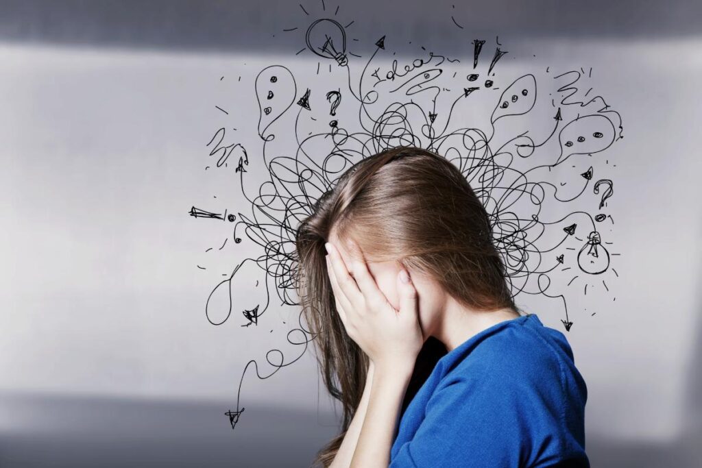 a person puts their face in their hands in profile with a drawing of squiggles coming out of their head to show the common causes of anxiety