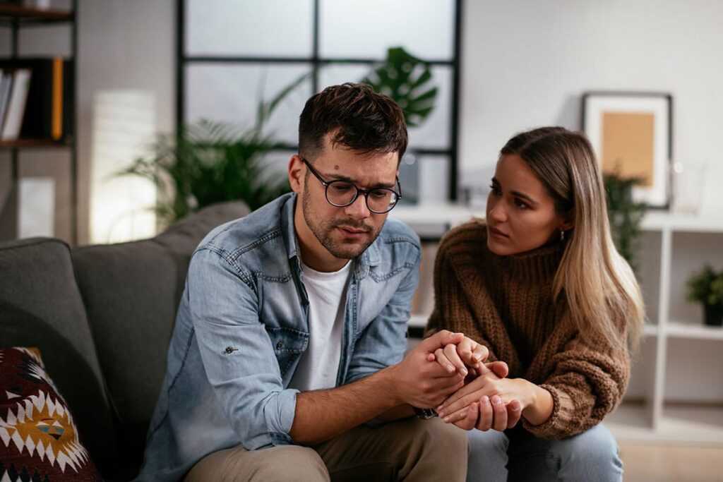 a couple sits on a couch holding hands talking about recovery from alcoholism