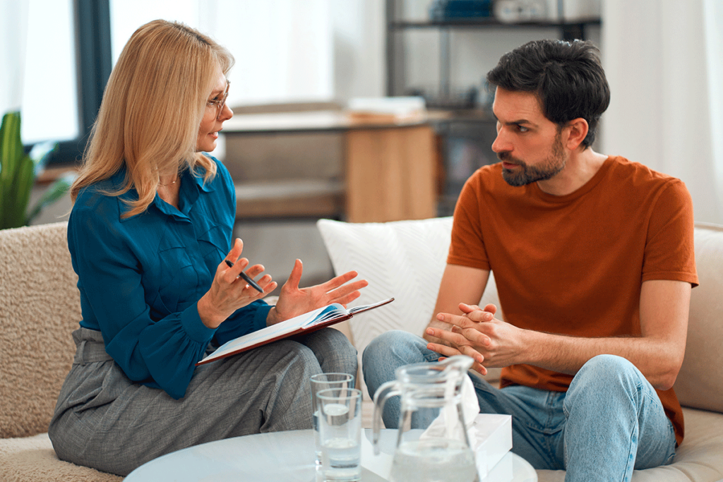 A man sits across from a counselor and understands the benefits of addiction therapy.