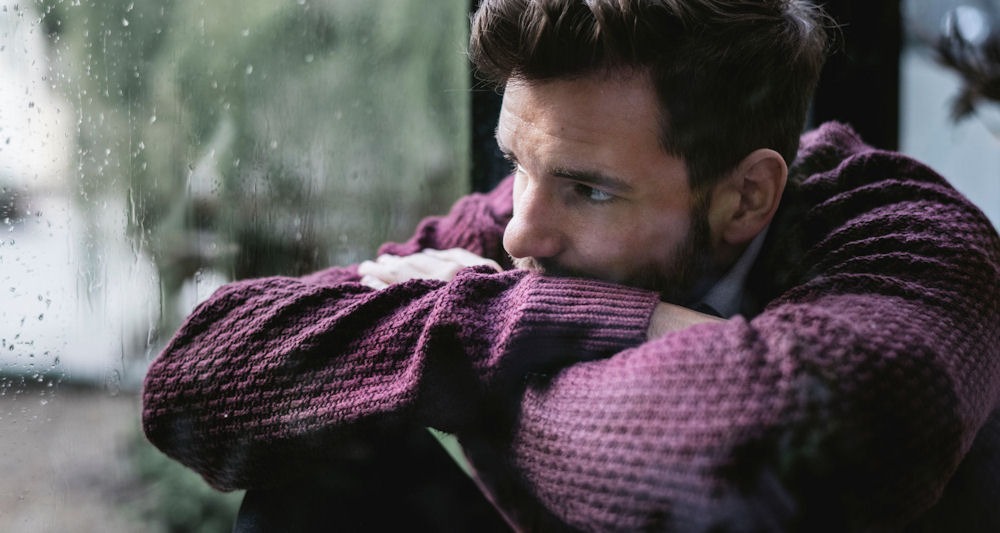 Man sitting pensively by the window, symbolizing the challenges of a high functioning alcoholic